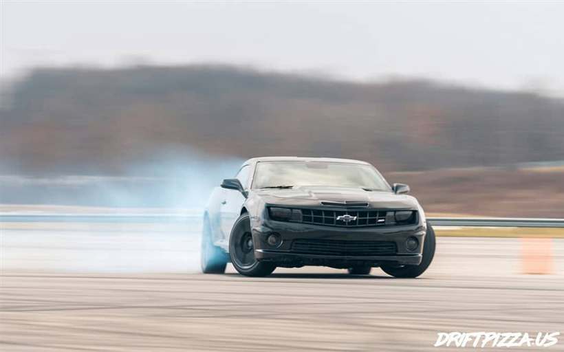 The Camaro trailing blue-white tyre smoke on a cold day with bare Pennsylvania hills behind.