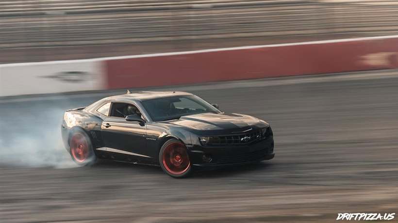 The Camaro on red wheels sliding along a banked wall in warm evening light.