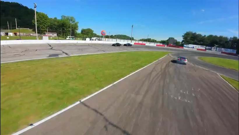 Aerial view of the car drifting around an oval, green infield and Pennsylvania hills beyond.